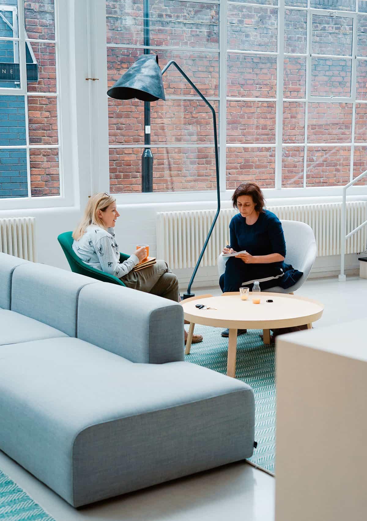 Light-filled room with a grey sofa and two people talking at a round table